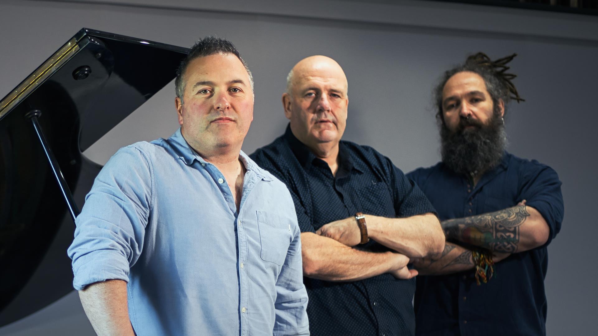 Picture of the three Irish vocalists Ger, Trevor and Don standing by a piano