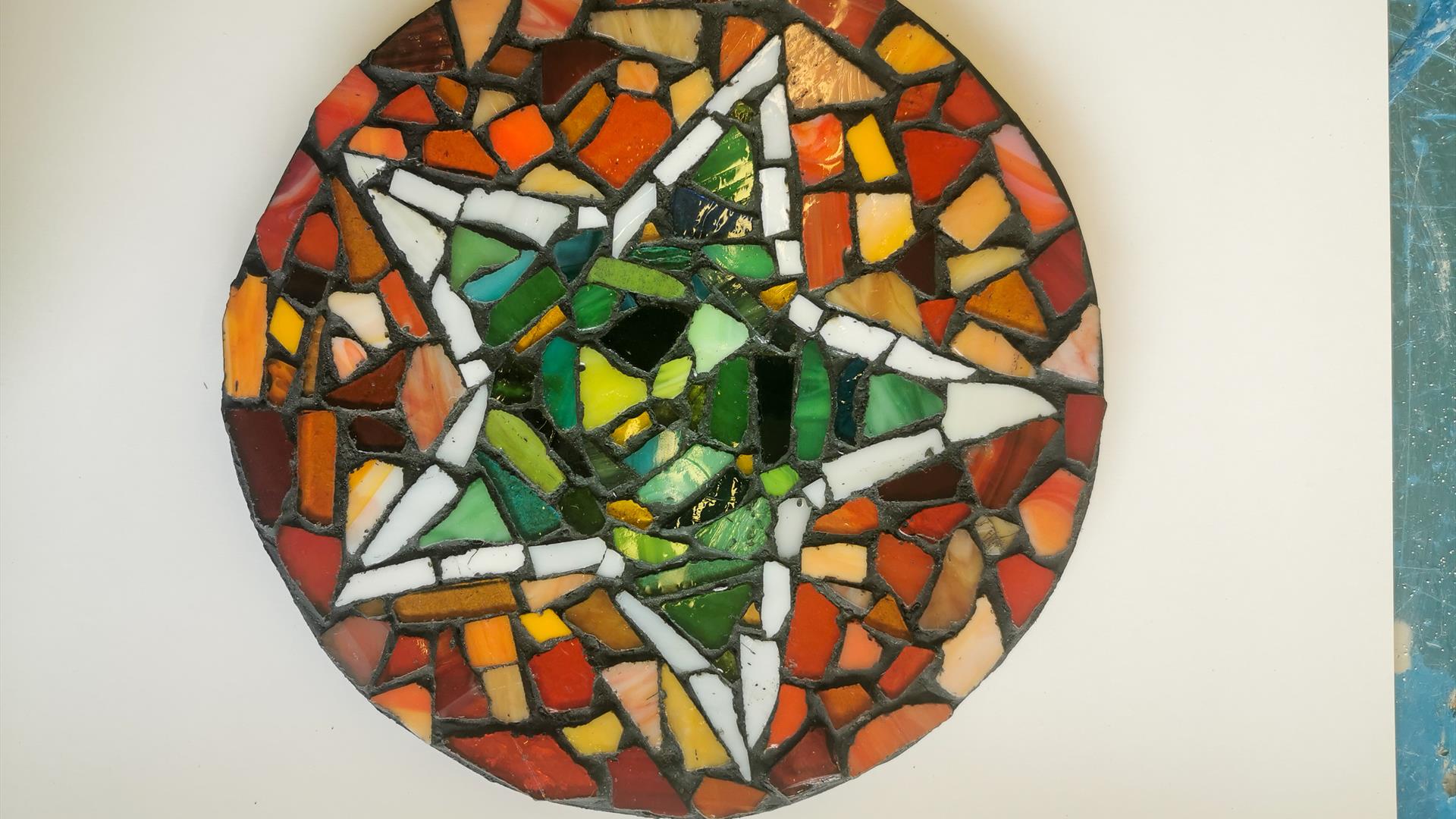 Image showing circular mosaic, with green shards of pottery making a star, white shards of pottery bordering the star, and orange shards making up the