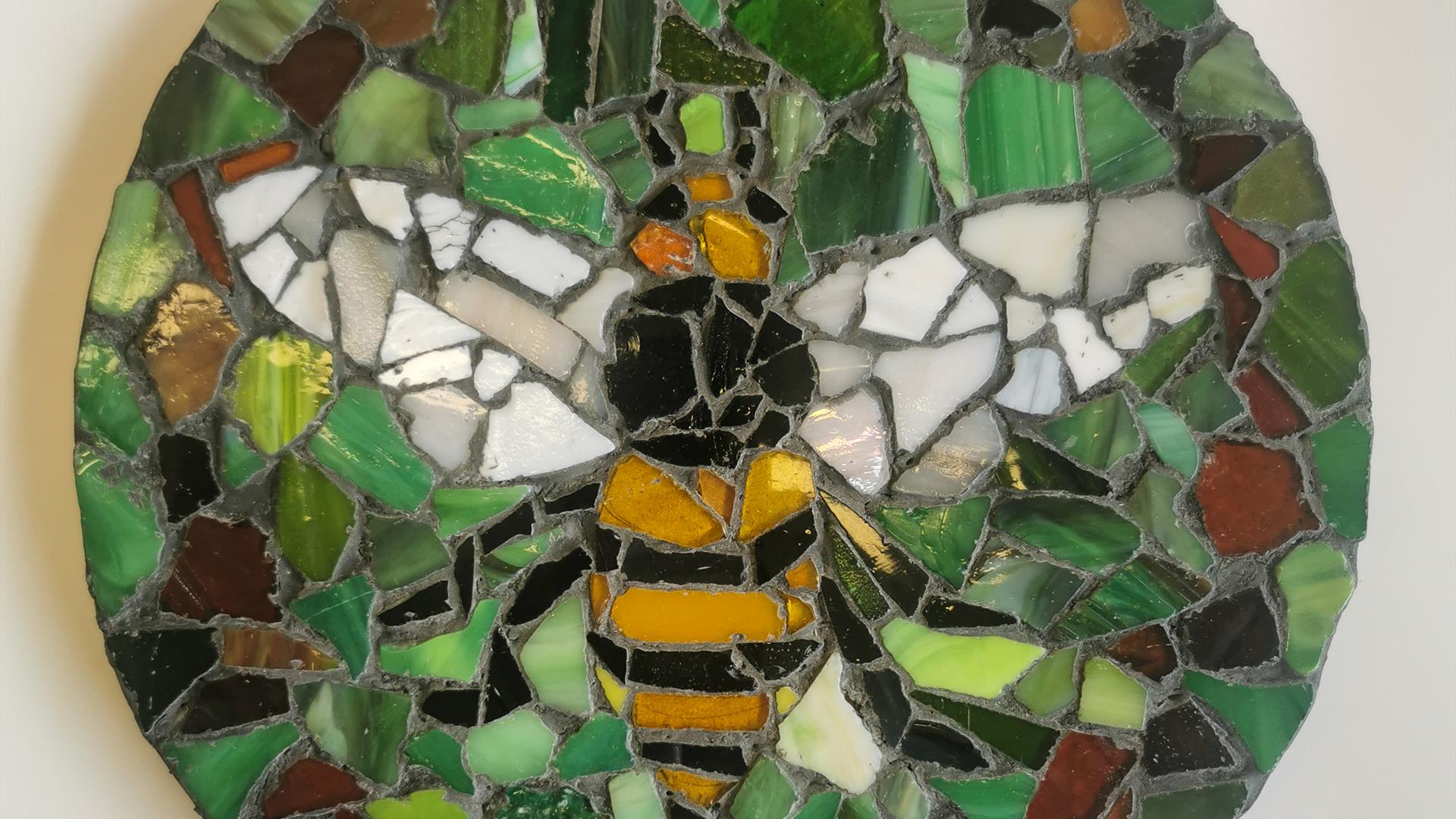 Completed circular mosaic with yellow, black and white pottery shards creating a bee and green and brown shards completing the background.