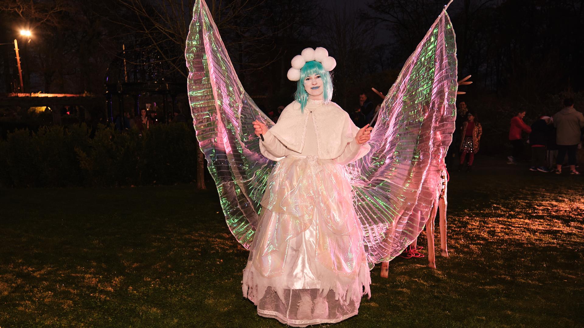 A woman dressed as a Christmas fairy is holding out her wings