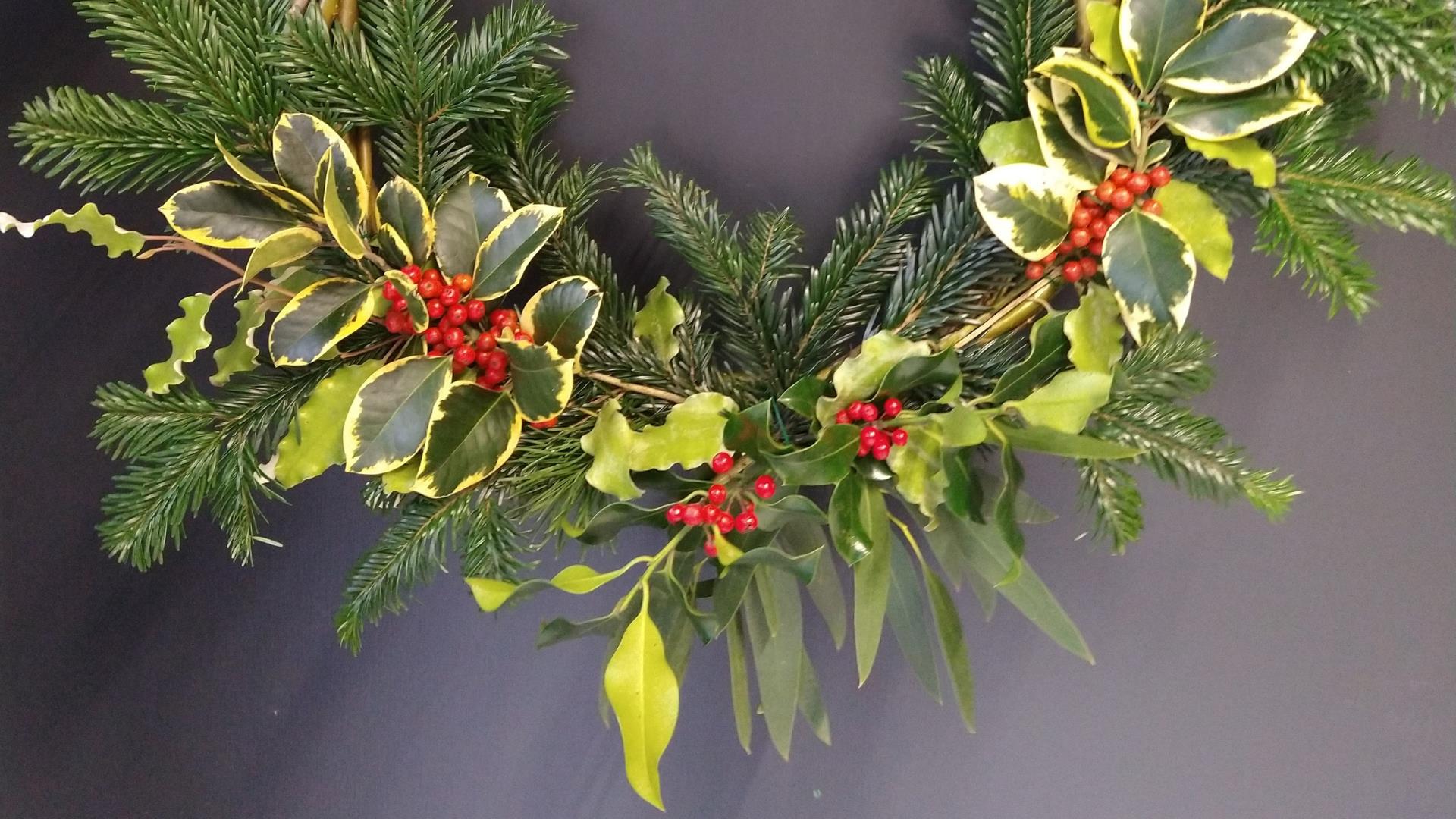 Image of Christmas wreath made using pine tree branches and holly plants.