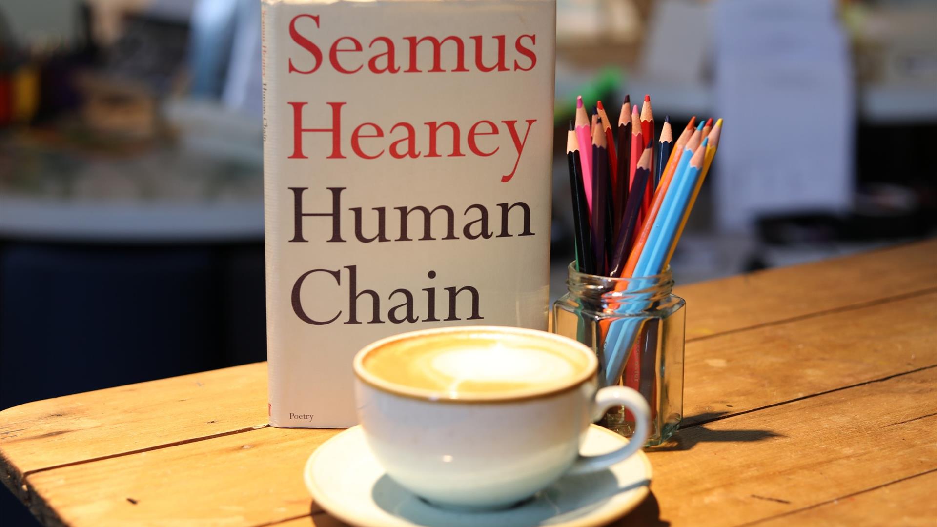 Seamus Heaney Human Chain book propped up behind a cup of milky coffee with a jar of coloured pencils