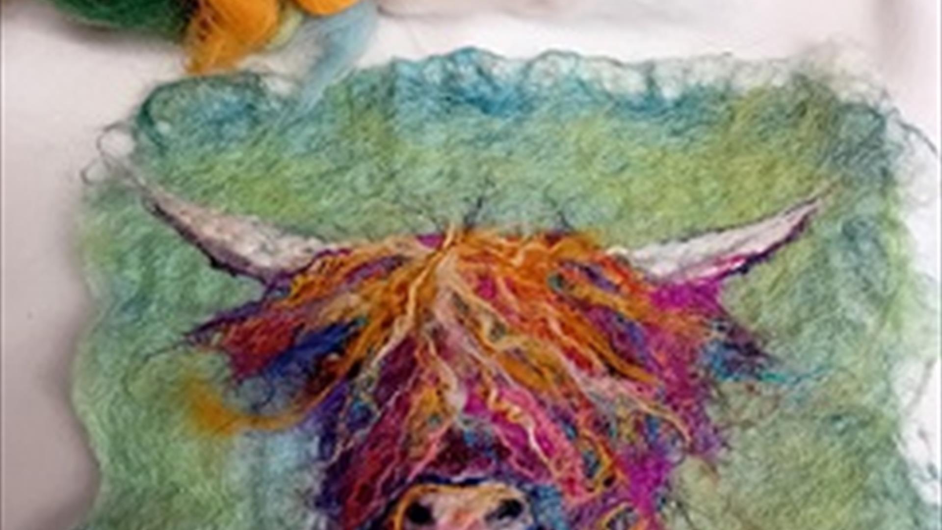 A small piece of felt craft using orange and purple hews to create an image of a highland cow's head against a moss green background.