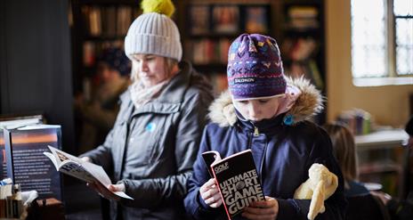 Two people with coats and hats on looking at books