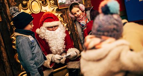 Santa on his chair with a girl and boy on either side reading letters