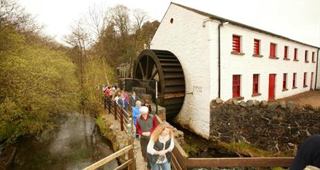 A group of people walking past the water wheel at Wellbrooke