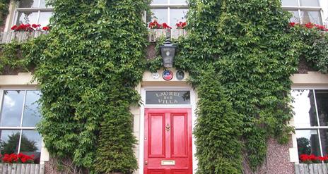 Outside image of Laurel Villa with greenery on walls and red door