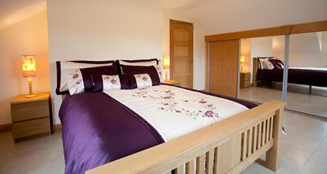 Double bedroom with sliding mirror wardrobe doors, double bed and bedside lockers