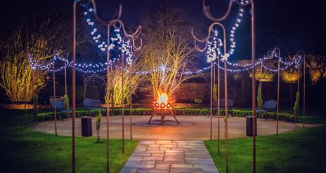 Paved path leading to circular patio with fairy lights and fire pit.