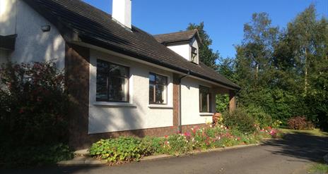 Image of a cream bungalow with flower beds and tress surrounding it