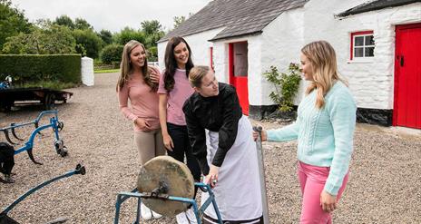 Girls pictured with a woman in period dress outside an old thatched cottage with a red door