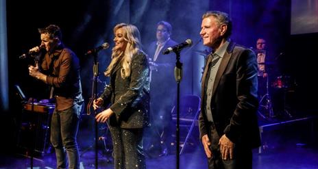 An image of Johnny Brady, Claudia Buckley and John Hogan on stage singing