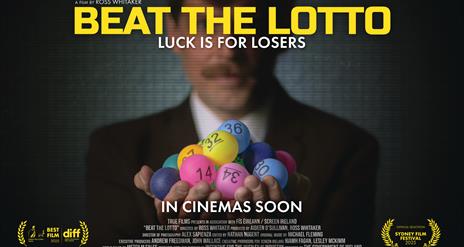 Image of gentleman in suit holding bright coloured lottery number balls