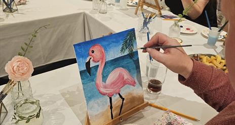 H shaped table with people painting a pink flamingo