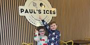 Two children pointing to a Pauls Ices Cafe sign