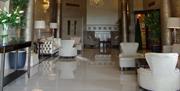 Image of the entrance hall with shiny tiled floors, cream armchairs, gold metallic columns and patterned wallpaper