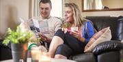 Happy couple sitting on a sofa reading the brochure and drinking tea