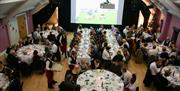 A large group of people at at sit down dinner with sport showing on a big screen