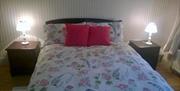 Double bed bedroom with floral bedding and 2 bedside lockers with lamps
