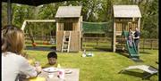 wooden play area with slide, swings and bridge.  Image shows family eating and play on slide