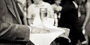 Black and white image of a waiter holding a champagne flute on a tray