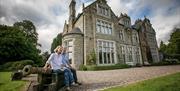 A couple sitting on an old canon in front of a large 17th century manor house