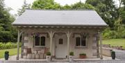 Blessingbourne Gate Lodge with white front door and 2 windows.  Hanging flowers and plant around the front of the lodge with outside table and 2 chair