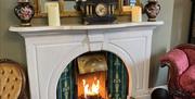 A lit fire with white mantle, vases and a gold mirror on top