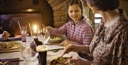 Mother and daughter having a meal in a restaurant in front of an open fire.