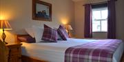 This double room features a comfortable double bed with purple plaid accents, bedside tables, a dresser with warm lighting, and an ensuite with a show