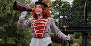 Girl dressed as circus master with loud speaker saying roll up