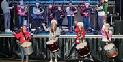 Members of Tullylagan Pipe Band are performing on and  in front of a brightly lit stage