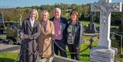 Tour group standing in front of large white marble cross and embellished with roses, Rose Kavanagh's grave