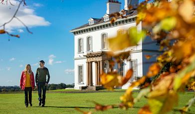 A couple walking through gardens of Ballyscullion park with the Georgian House in the background.