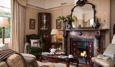 A cosy lounge set up at Ardtara house, showing a lit, open fire and a serving of afternoon tea.