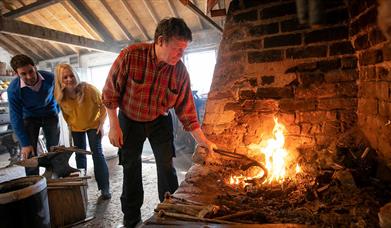 A blacksmith at the fire with a couple looking on