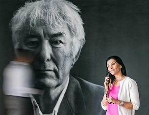 A woman in front of a large black and white image of Seamus Heaney's face