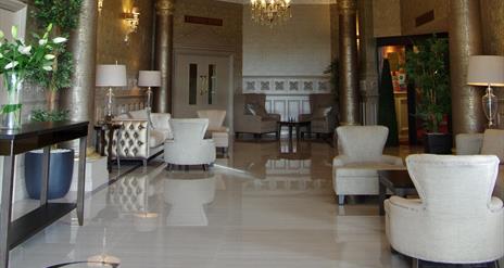 Image of the entrance hall with shiny tiled floors, cream armchairs, gold metallic columns and patterned wallpaper