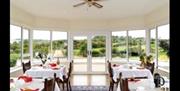 Dining area with several tables and 2 chairs.  Full window walls with scenic view