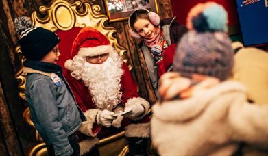 Santa on his chair with a girl and boy on either side reading letters