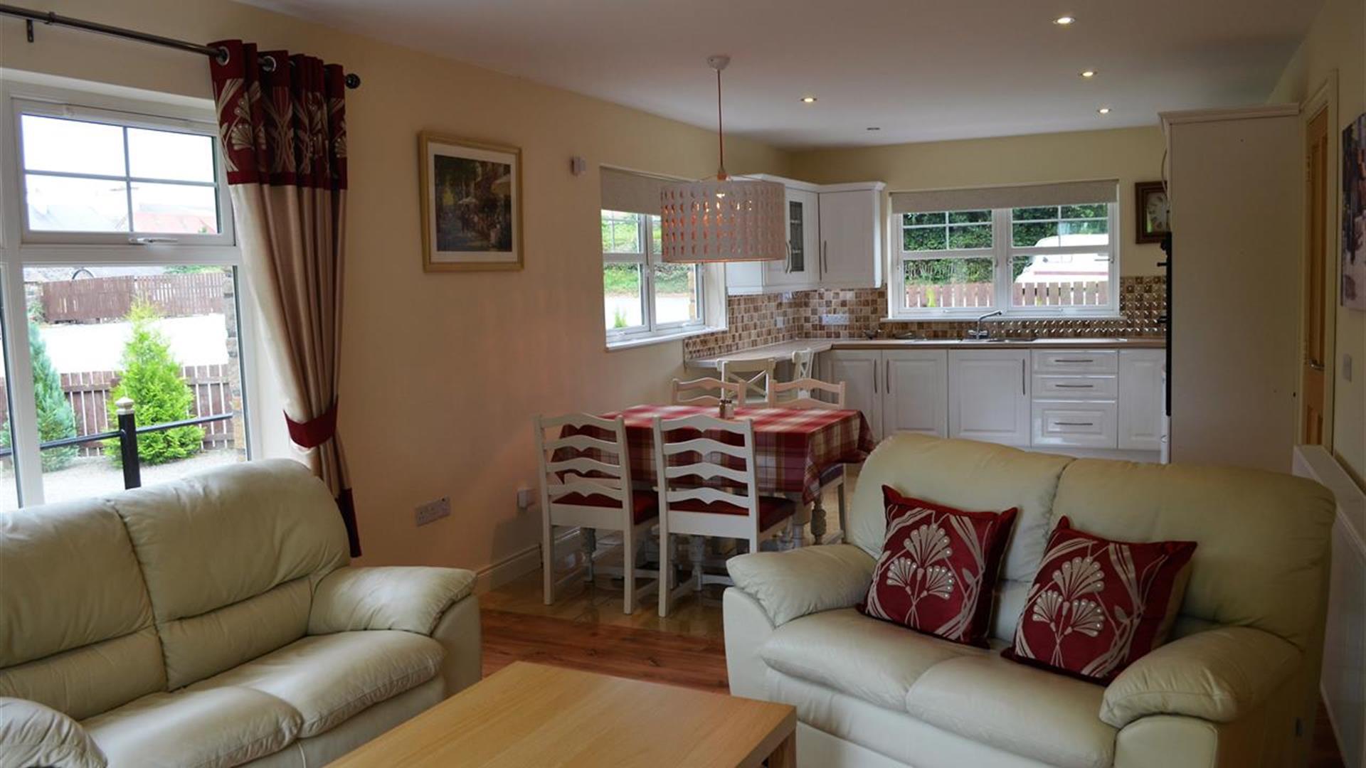 Open plan kitchen, dining and living area with 2 cream 2 seater sofas and dining table with 4 chairs