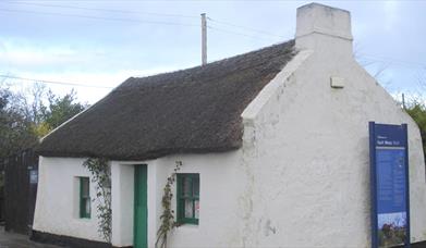 Image of a white cottage with a thatched rood and green door