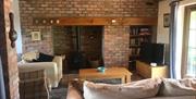 Living room with brick accent wall, a wood burner, TV, bookcase with books, two sofas and an arm chair