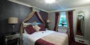 Double bed with coloured cushions and throw, matching curtains, bedside lockers and patterned wallpaper