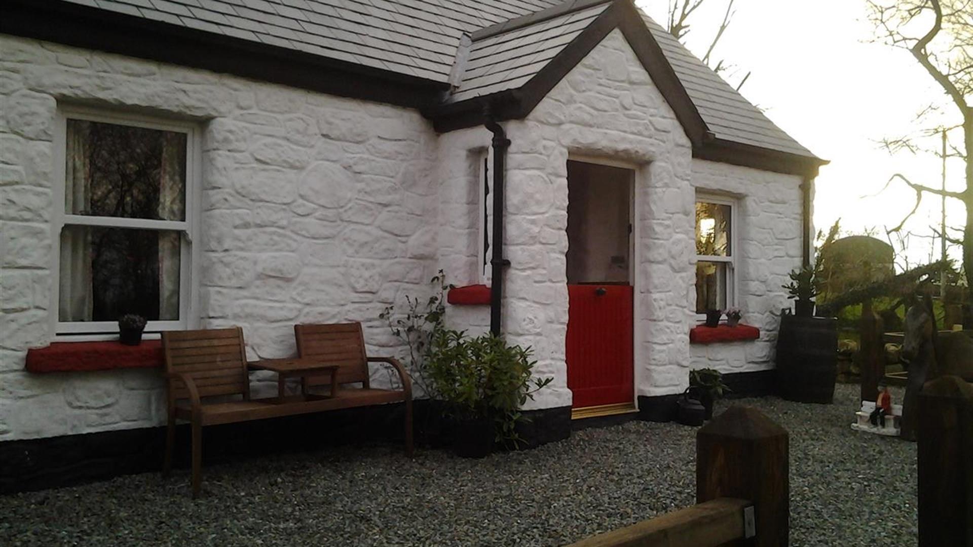 Outside view of cottage with red door and wooden chairs at front