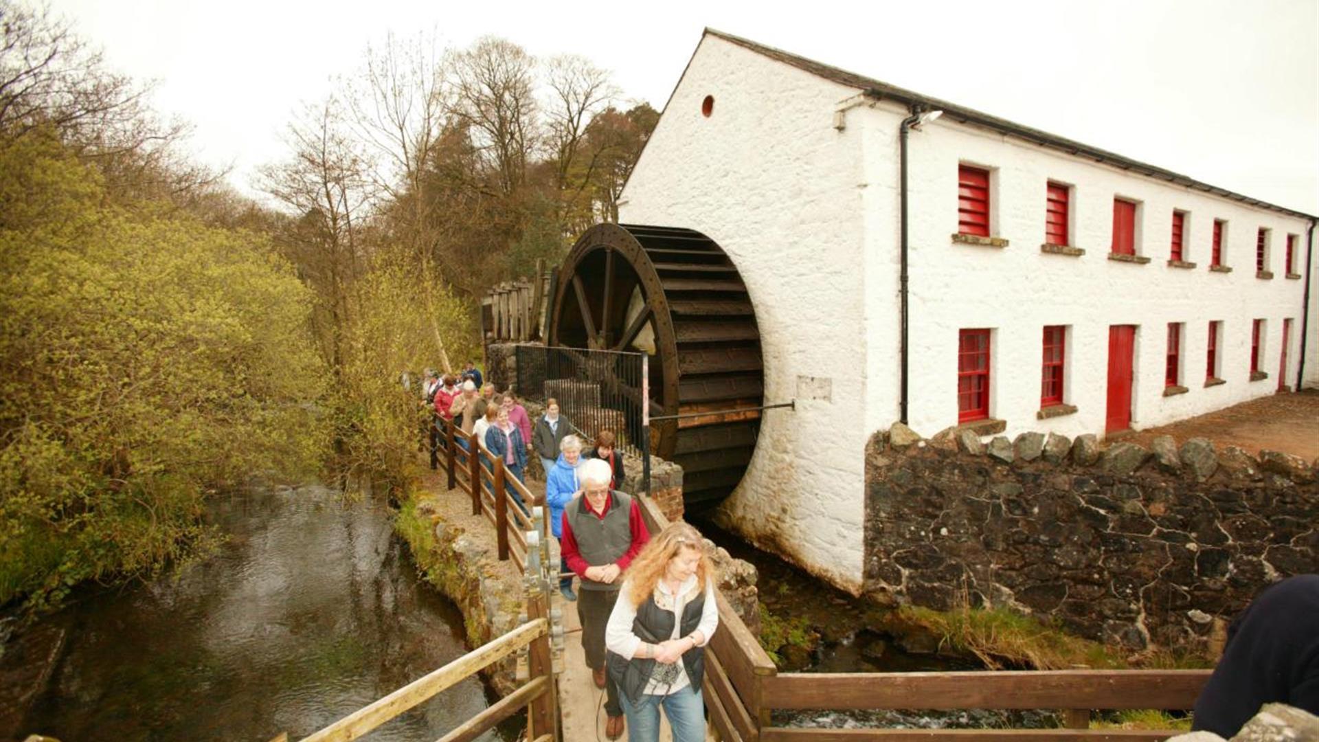 A group of people walking past the water wheel at Wellbrooke