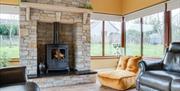 Large stone surrounding fireplace with wood burning stove in a sun room with many windows