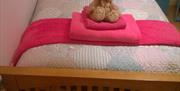 Single wooden bed with pink towels and teddy bear on top