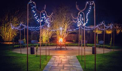 Paved path leading to circular patio with fairy lights and fire pit.