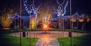 Paved path leading to circular patio with fairy lights and fire pit.